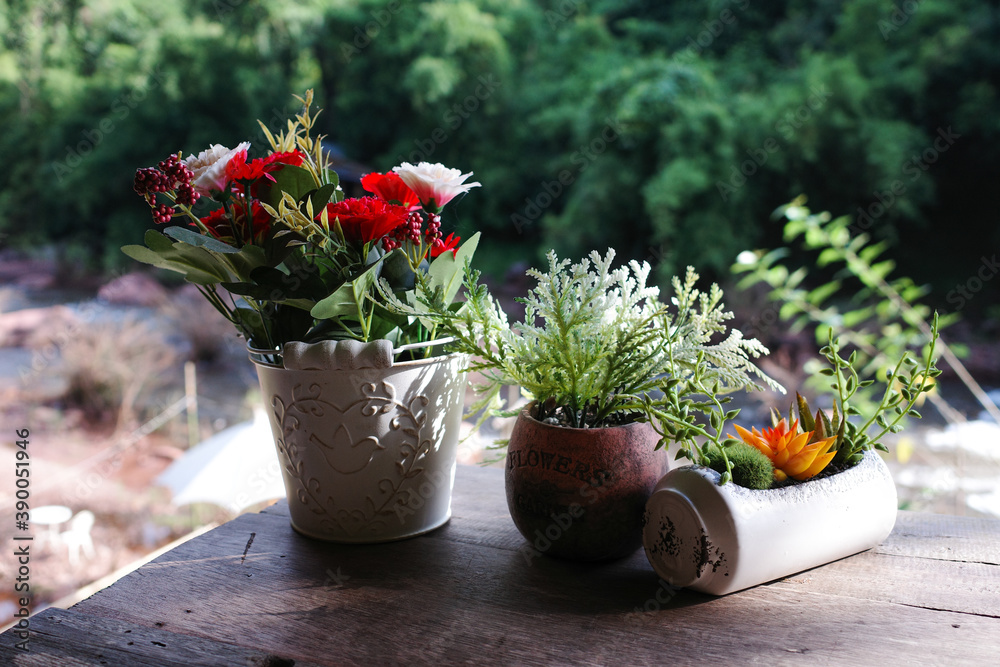 Focus on colorful artificial flowers in a small pot on the wooden table With blurred background
