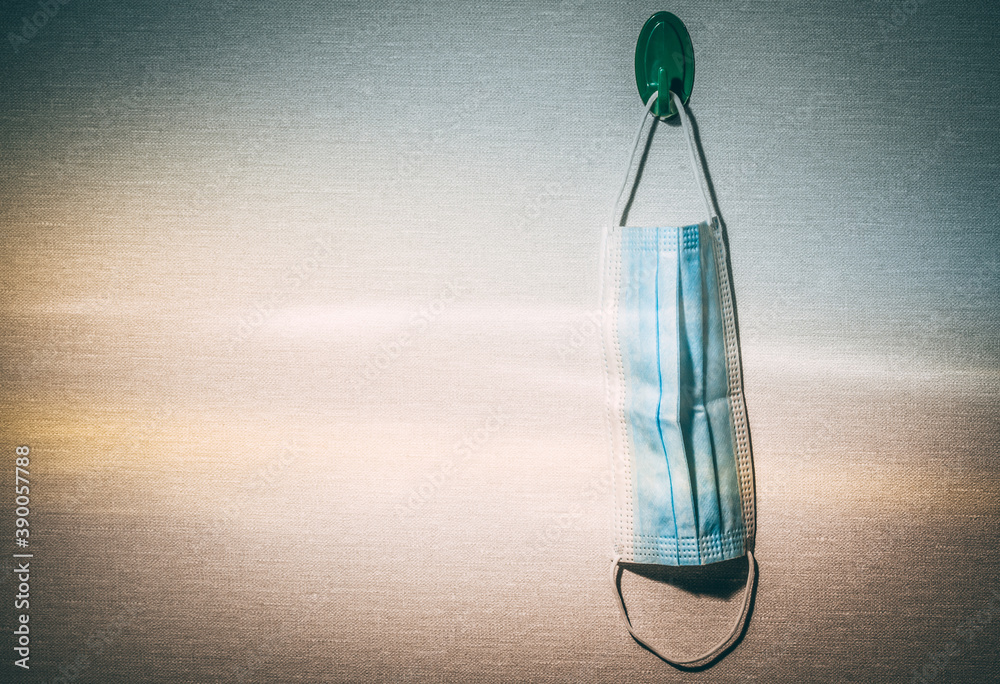 Closeup of a surgical mask hanging from a hook on a wall. Covid-19 reusing medical supplies concept.
