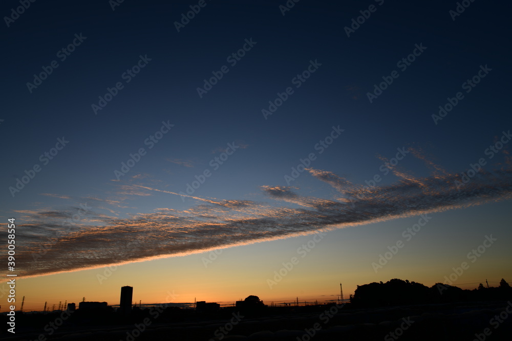 夜明けの空に現れた龍のしっぽのような鱗雲。空を二分する巻積雲。朝焼け。空の背景素材