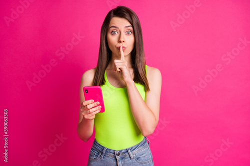 Photo of funny young lady forefinger lips hold telephone wear green singlet isolated vivid pink color background