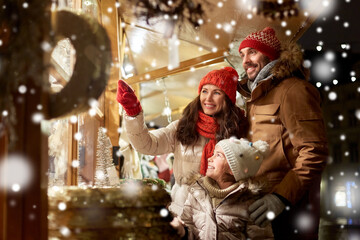 family, winter holidays and celebration concept - happy mother, father and little daughter at christmas market on town hall square in tallinn, estonia over snow