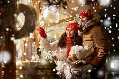 family, winter holidays and celebration concept - happy mother, father and little daughter at christmas market on town hall square in tallinn, estonia over snow