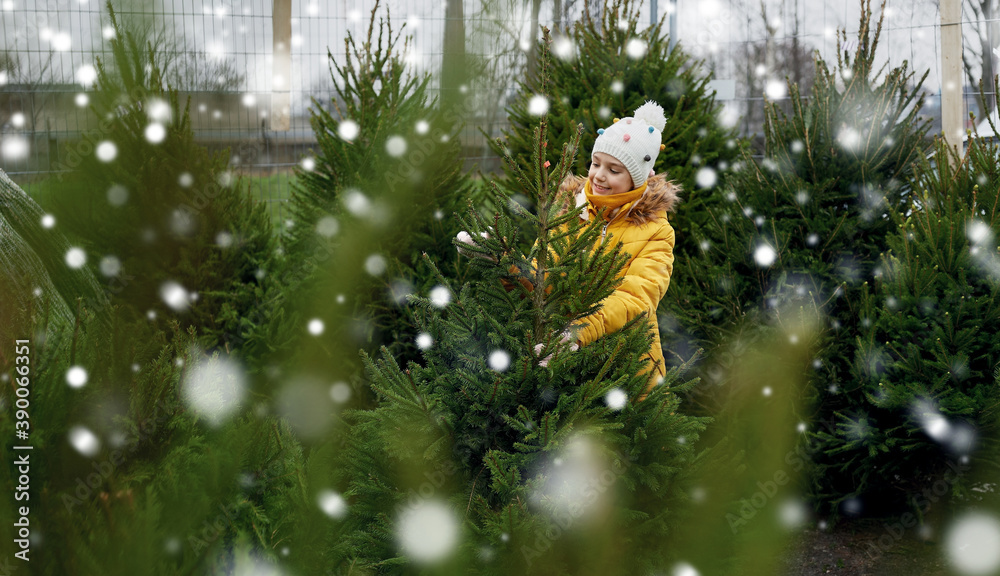 winter holidays and people concept - happy smiling little girl choosing christmas tree at street market over snow
