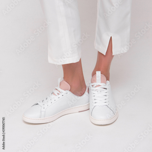 close-up female white sneakers of young girl in white pants which is standing on the white wall background. lifestyle medical concept. free space , mockup