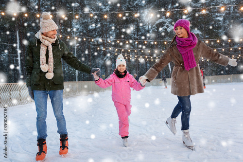 christmas, family and leisure concept - happy mother, father and daughter at outdoor skating rink in winter over snow