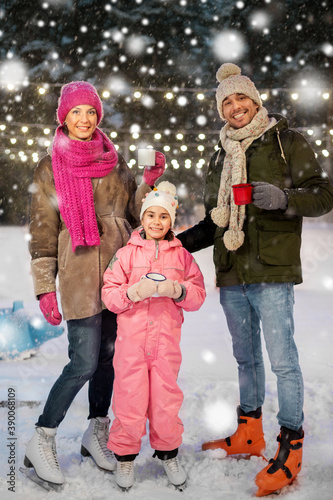 christmas, family and leisure concept - happy mother, father and daughter drinking hot tea at outdoor skating rink in winter over snow