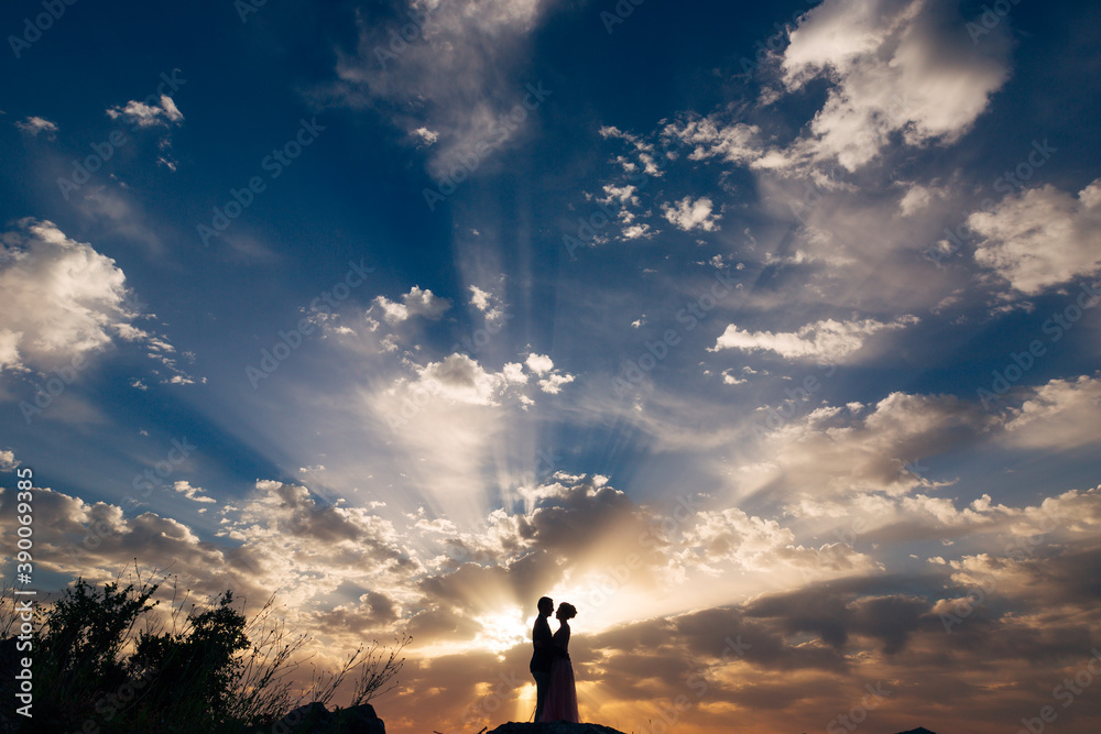 the bride and groom tenderly hug on the mountain in the rays of the setting sun