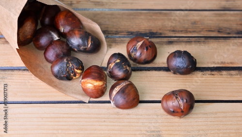 roasted chestnuts  in a papaer bag spilled on wooden table