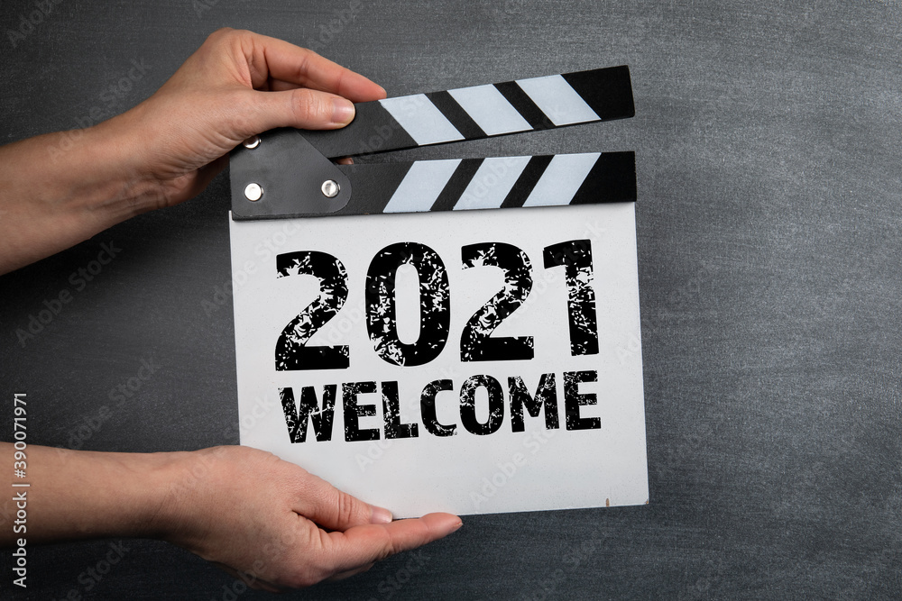 2021 WELCOME. Movie clapper in woman hand. Black chalk board background