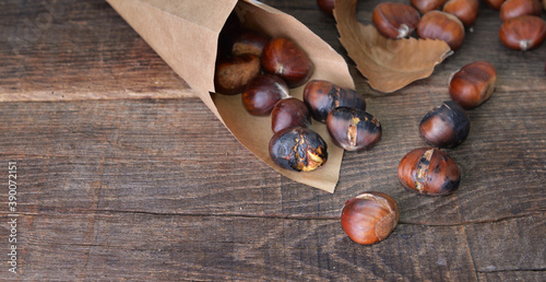 roasted chestnuts  in a papaer bag spilled on wooden table