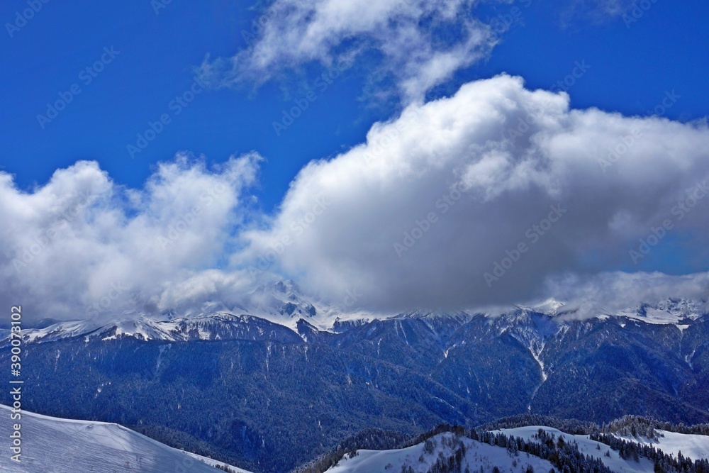 Beautiful winter landscape in the mountains, deep snow, blue sky, ski slopes, winter forest, snow-capped mountain peaks.