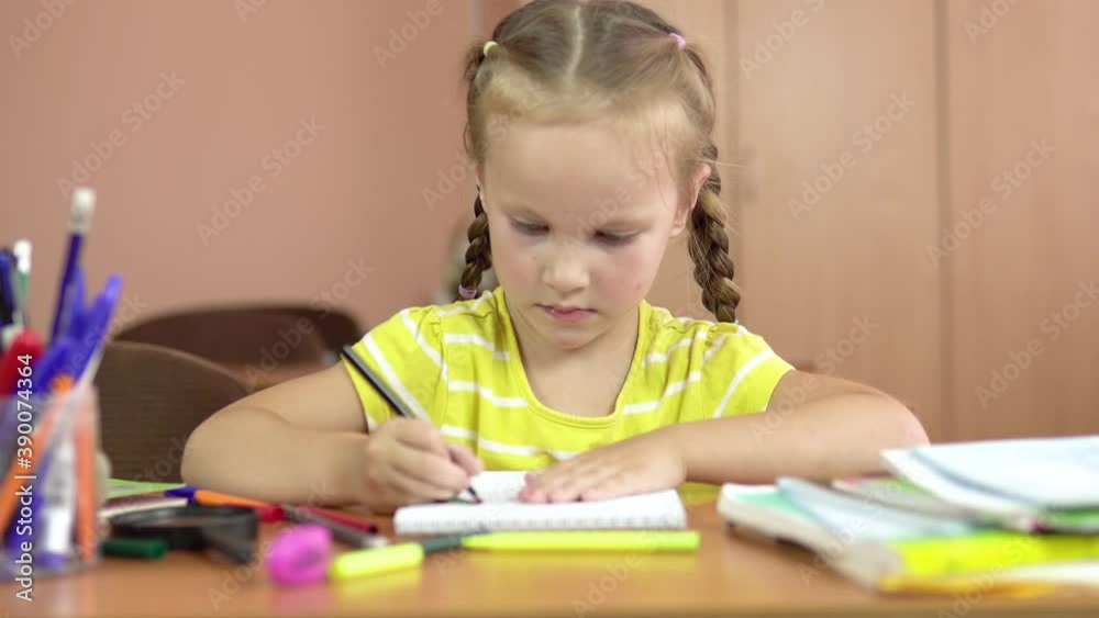 Little cute girl sits at a desk in the classroom. Draws in a notebook with a felt-tip pen. Preschool education. 4k Little cute girl sits at a desk in the classroom. Draws in a notebook with a felt-tip pen. Preschool education. 4k