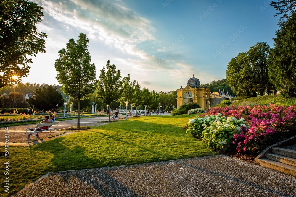Marianske Lazne / Czech Republic - August 8 2020: View of the Maxim Gorky colonnade and singing water fountain. Colorful flowers, green lawn. Summer sunset in famous spa city with blue sky and clouds.