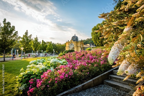 Marianske Lazne   Czech Republic - August 8 2020  View of the Maxim Gorky colonnade and singing water fountain over pink and white flowers. Summer evening in famous spa city with blue sky and clouds.