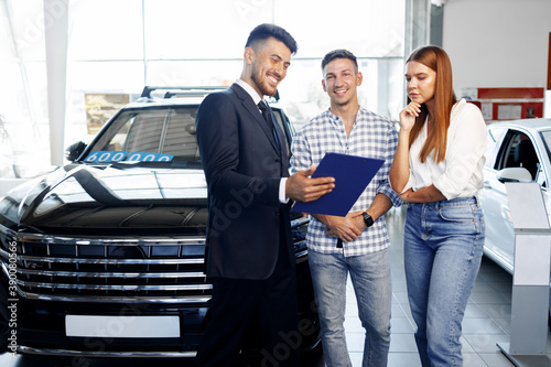 Man car salesman telling about the features of the new car to the couple