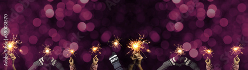 New Year / Silvester Party background banner greeting card - Group of happy people / family holding sparkling sparklers in her hands at dark night, with pink bokeh lights