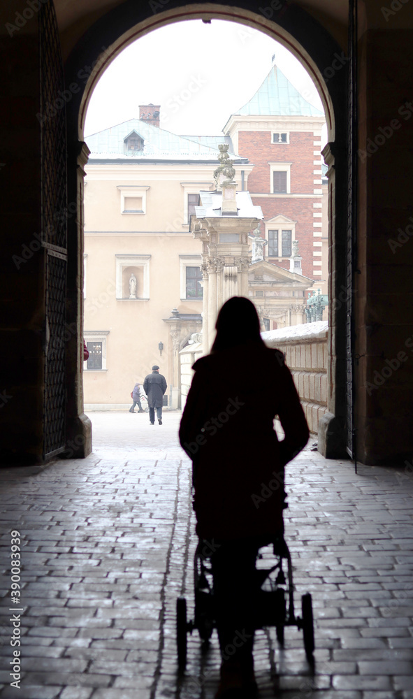 Silhouette of a woman pushing a stroller towards a gate on Wawel Castle hill in Poland, Krakow Silhouette of a woman pushing a stroller towards a gate on Wawel Castle hill in Poland, Krakow
