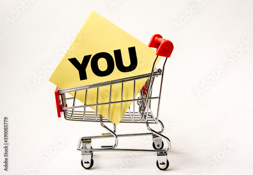 Shopping cart and text you on yellow paper note list. Shopping list, business concept on white background.