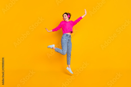 Full size photo of pretty funky lady jump high have fun listen earphones wear pullover isolated yellow color background