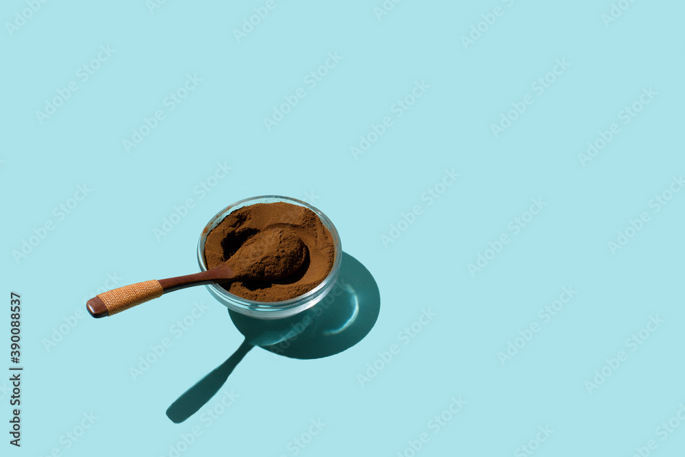 cinnamon powder in a glass plate with a wooden spoon on a blue background top view. for text space. Hard light harsh shadows cinnamon powder in a glass plate with a wooden spoon on a blue background top view. for text space. Hard light harsh shadows