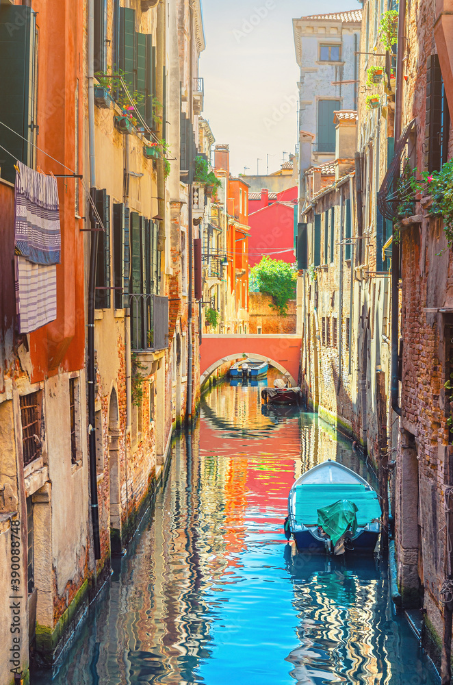 Venice cityscape with narrow water canal with boats moored between brick walls of old buildings and stone bridge, Veneto Region, Northern Italy. Typical Venetian view, vertical view