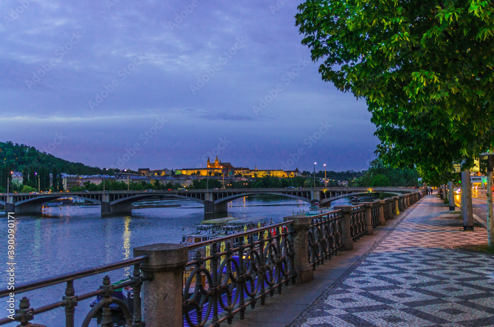 Obraz premium Prague with promenade riverside road, Prague Castle, St. Vitus Cathedral in Hradcany district, bridges over Vltava river, night evening twilight view, Bohemia, Czech Republic