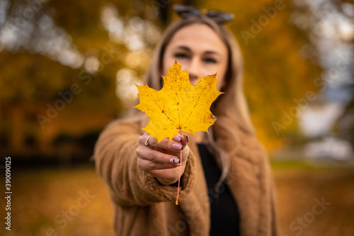 Portrait of a young smiling woman in the park on the blurred background. She is holding fallen leaves in his hand.