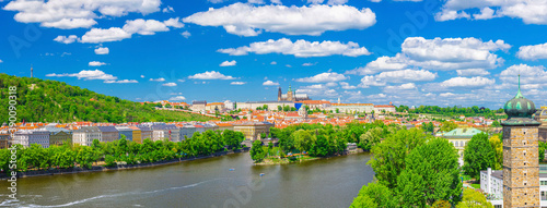 Panorama of Prague city historical centre with Prague Castle, St. Vitus Cathedral, Hradcany district, green hills and Vltava river, blue sky. Aerial panoramic view of Prague city, Czech Republic © Aliaksandr