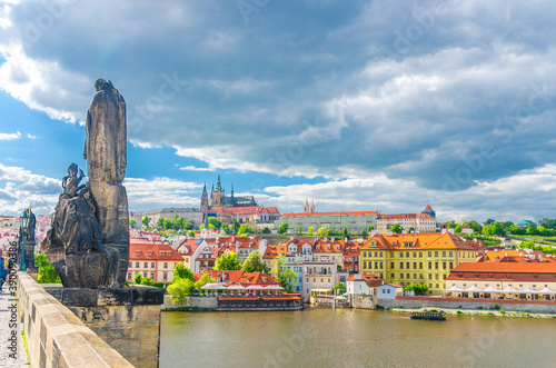 Saints Cyril and Methodius statue on Charles Bridge Karluv Most over Vltava river. Prague Castle, St. Vitus Cathedral in Hradcany district, blue sky white clouds background, Bohemia, Czech Republic