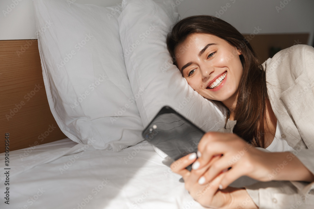 Beautiful woman lying in bed and checking phone. Girl browsing social networks while relaxing in bedroom Beautiful woman lying in bed and checking phone. Girl browsing social networks while relaxing in bedroom