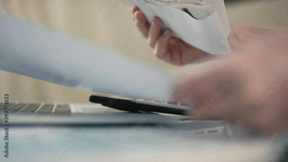 Closeup of female hands examining financial records counting sums at bills on calculator indoors Closeup of female hands examining financial records counting sums at bills on calculator indoors