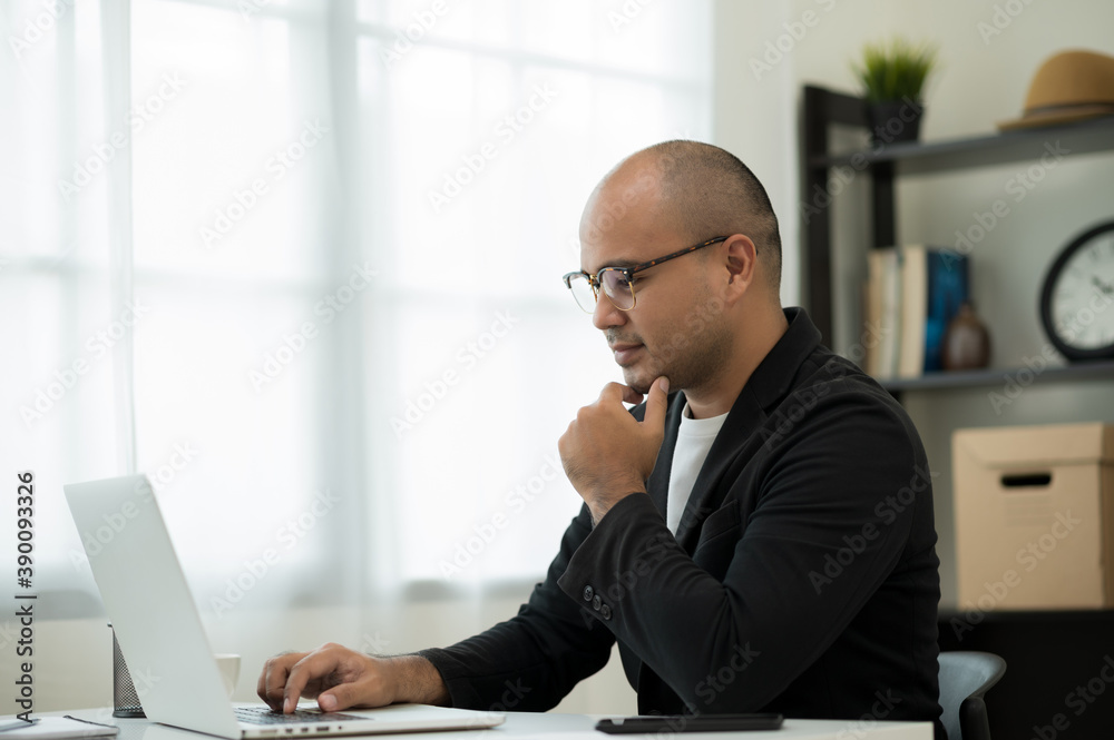 A middle-aged man around the age of 35. Working at home Work through the laptop by meeting video conference. He was wearing a black suit and glasses. Smiling asian businessman work from home.