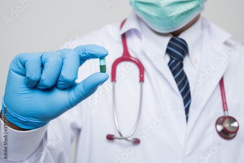 Close Up Asian bald Doctor in white coat, stethoscope, blue glove wearing.face mask holding a pills isolated on white background.