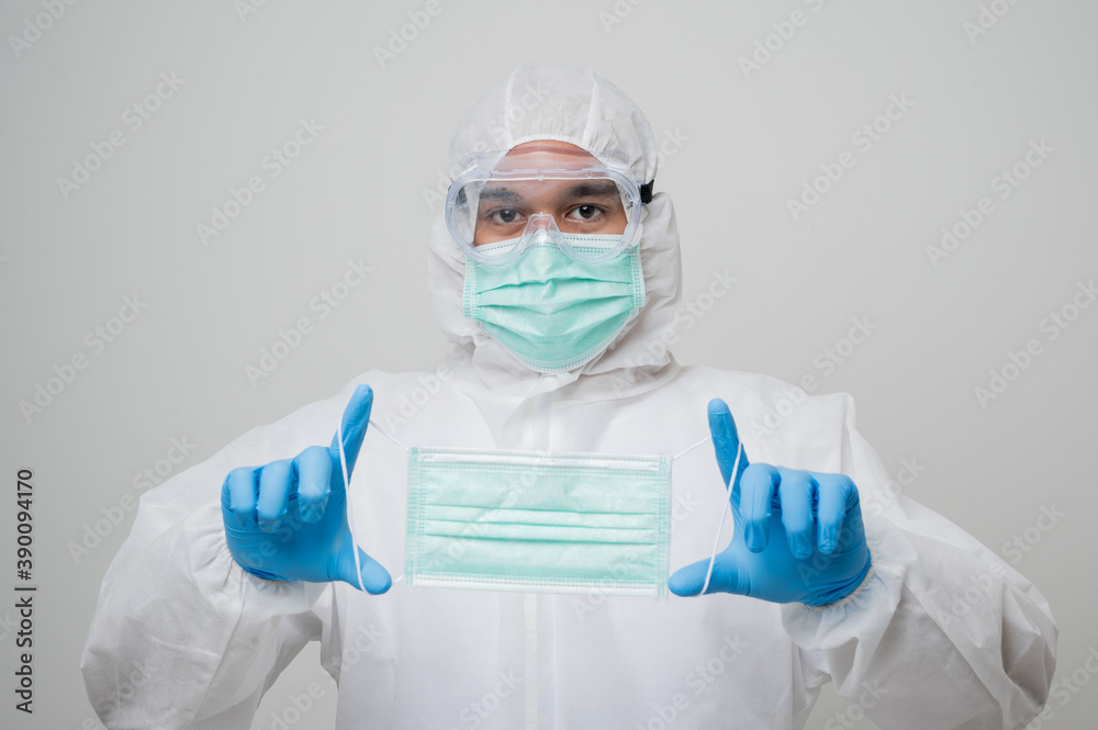 A portrait of virologist put on PPE suit showing a face mask with both hand isolated on white background. Personal Protective Equipment Concept.. A portrait of virologist put on PPE suit showing a face mask with both hand isolated on white background. Personal Protective Equipment Concept..