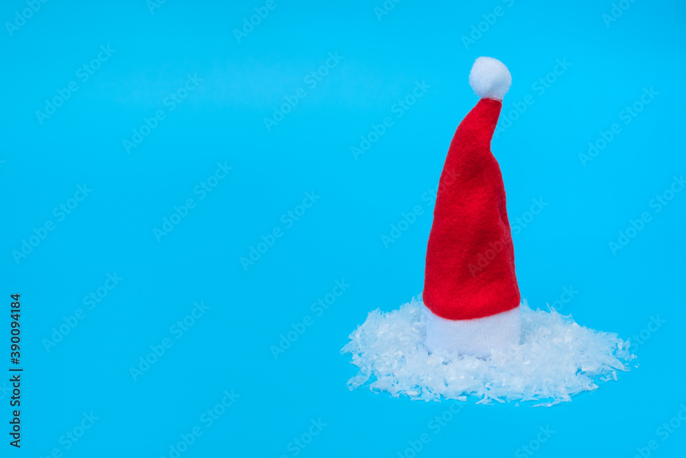 Santa Claus hat on snow against pastel blue background. Minimal winter concept. Christmas or winter greeting card, poster. New Year holiday. Santa Claus hat on snow against pastel blue background. Minimal winter concept. Christmas or winter greeting card, poster. New Year holiday.