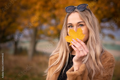 Young happy woman with a smile holds an autumn yellow leaf near the face.