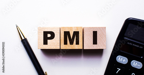 PMI is written on wooden cubes between a pen and a calculator on a light background. photo