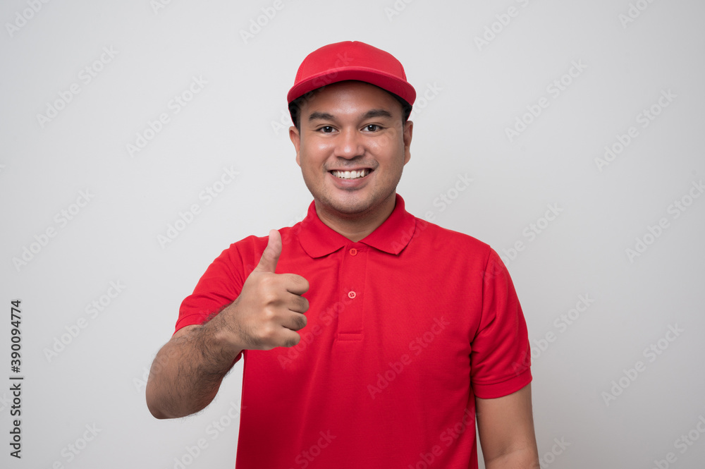 Smiling young handsome asian delivery man in red uniform standing with thumbs up on isolated white background. Smiling young handsome asian delivery man in red uniform standing with thumbs up on isolated white background.