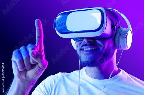 Afro american man wearing VR glasses in neon light against purple background