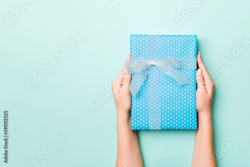 Woman hands give wrapped christmas or other holiday handmade present in colored paper. Present box, decoration of gift on Blue table, top view with copy space