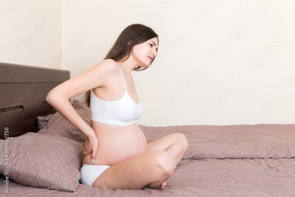 beautiful pregnant woman touching her tummy and keeping one hand on her back at home on bed beautiful pregnant woman touching her tummy and keeping one hand on her back at home on bed