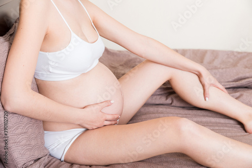 Pretty pregnant woman hands massaging leg sitting on bed © sosiukin