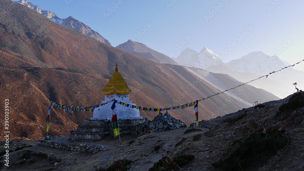 Buddhist monument (chorten) surrounded by mani stones and colorful prayer flags in the bright evening sun in Dingboche, Khumbu, Nepal on Everest Base Camp Trek in the majestic Himalayas.