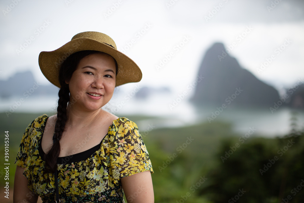 Asian woman wearing a floral dress, wearing a hat with a bright smile.