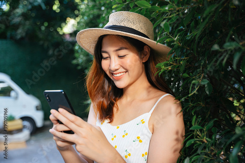 Cheerful asian woman wear hat chatting with smartphone outdoors.