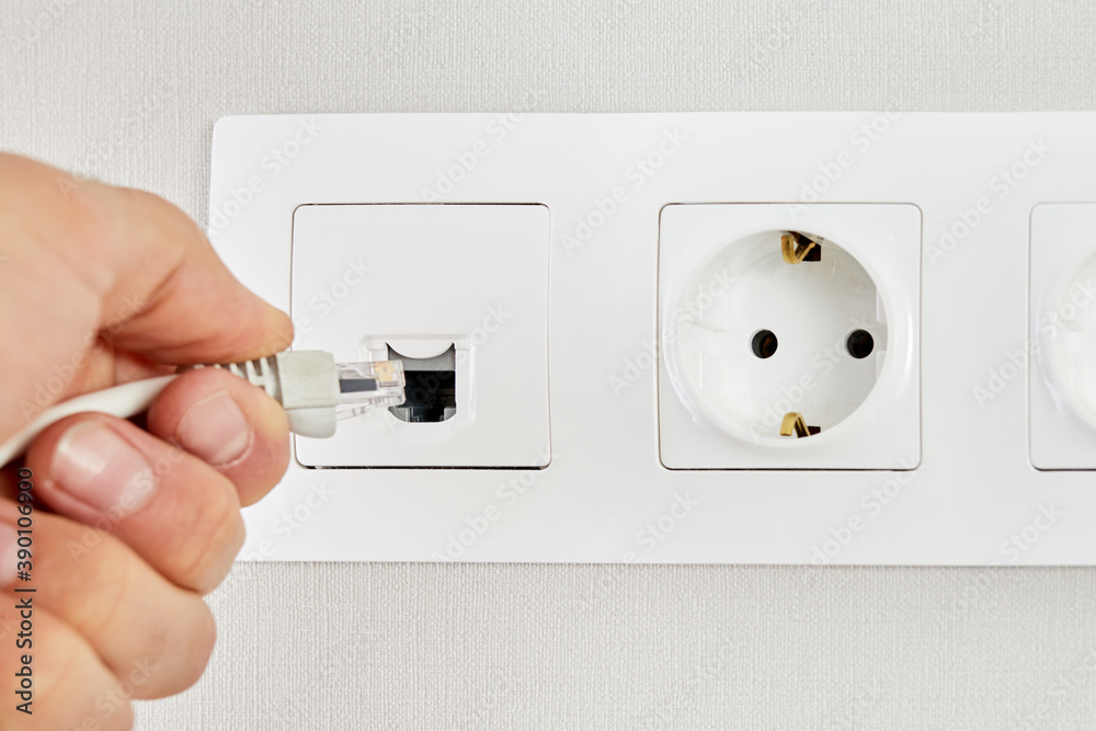 Close up of a man hand plugging an ethernet cable into a wall socket. Male hand puts network plug in the socket. Close up of a man hand plugging an ethernet cable into a wall socket. Male hand puts network plug in the socket.