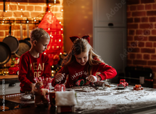 Young kids in winter sweaters making cookies in the kitchen with Christmas decor