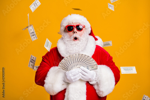Portrait of his he nice attractive amazed stunned fat overweight bearded Santa holding in hand throwing usd 100 fan cash salary deposit isolated bright vivid shine vibrant yellow color background