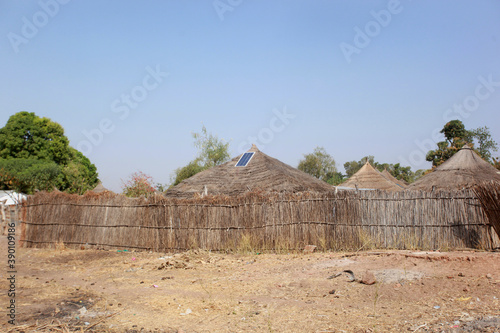 Basse region, Gambia, Africa - January 19, 2020, wide angle photography of traditional African round huts with  roofs made from high grasses, with a single solar panel on top of one hut,  on sunny day