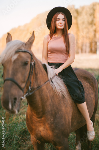 Girl in a hat riding a horse in nature.